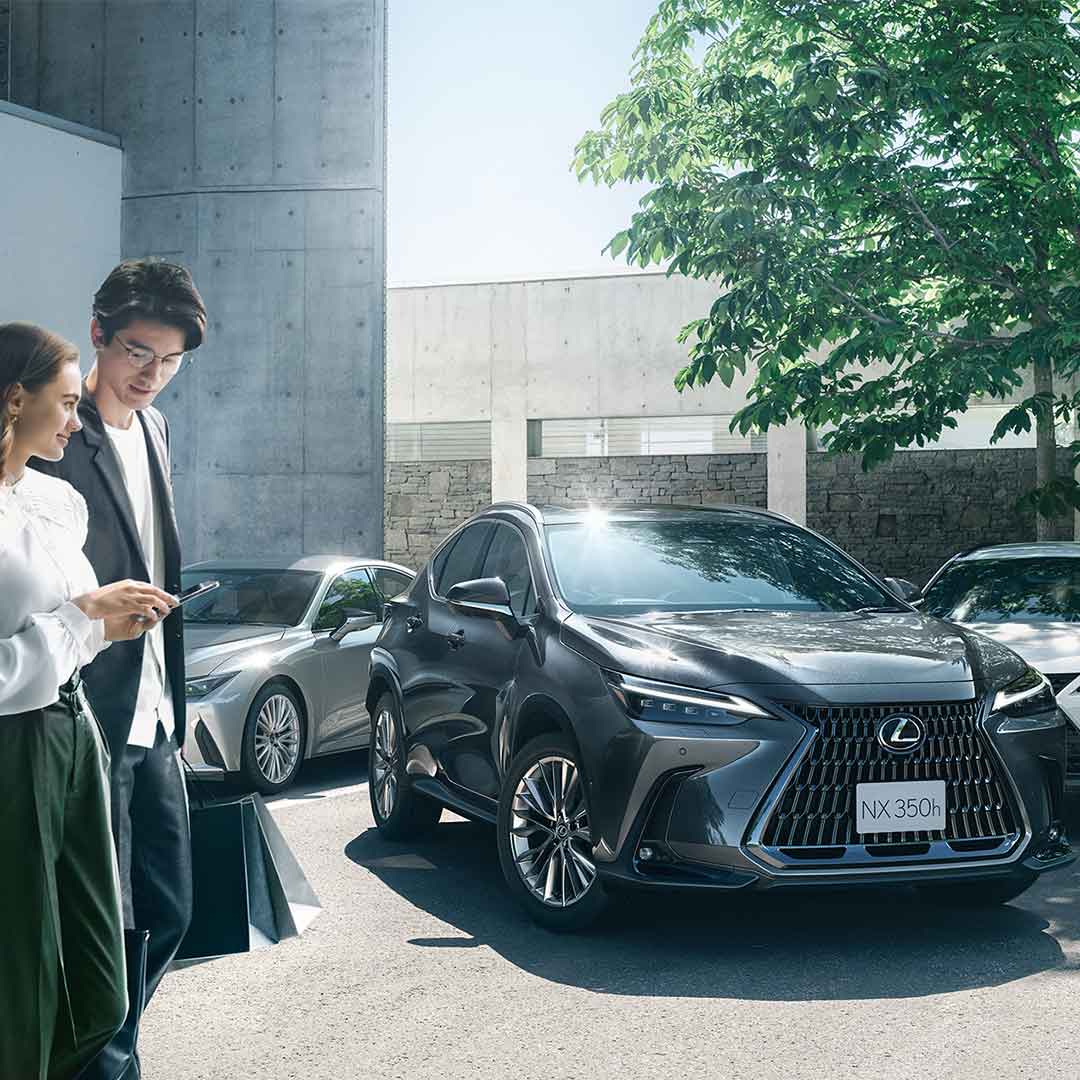 A woman and man stand with a smartphone as they watch the NX intelligently park.