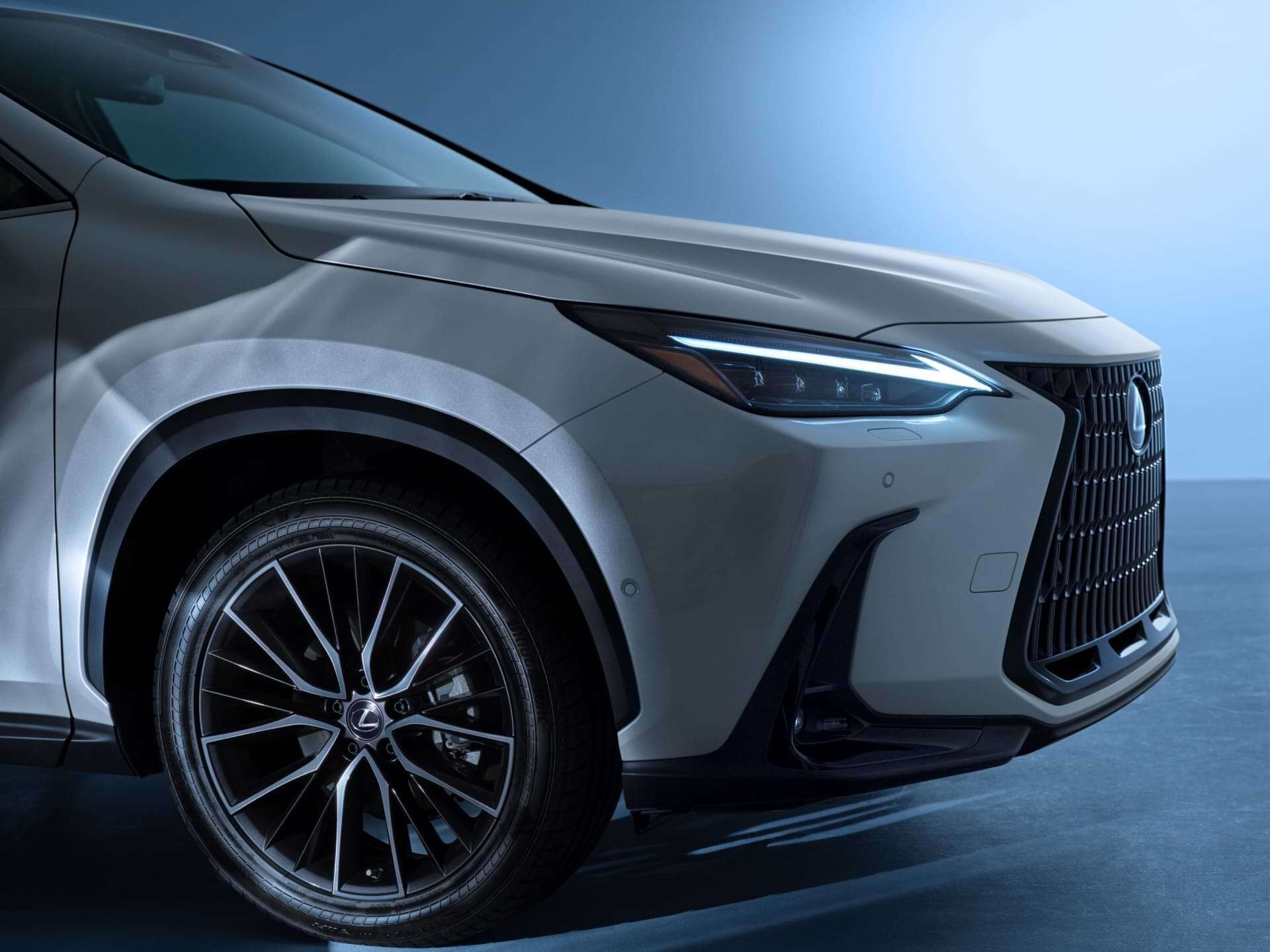 Front right wheel of a white NX as it sits with headlamps aglow.