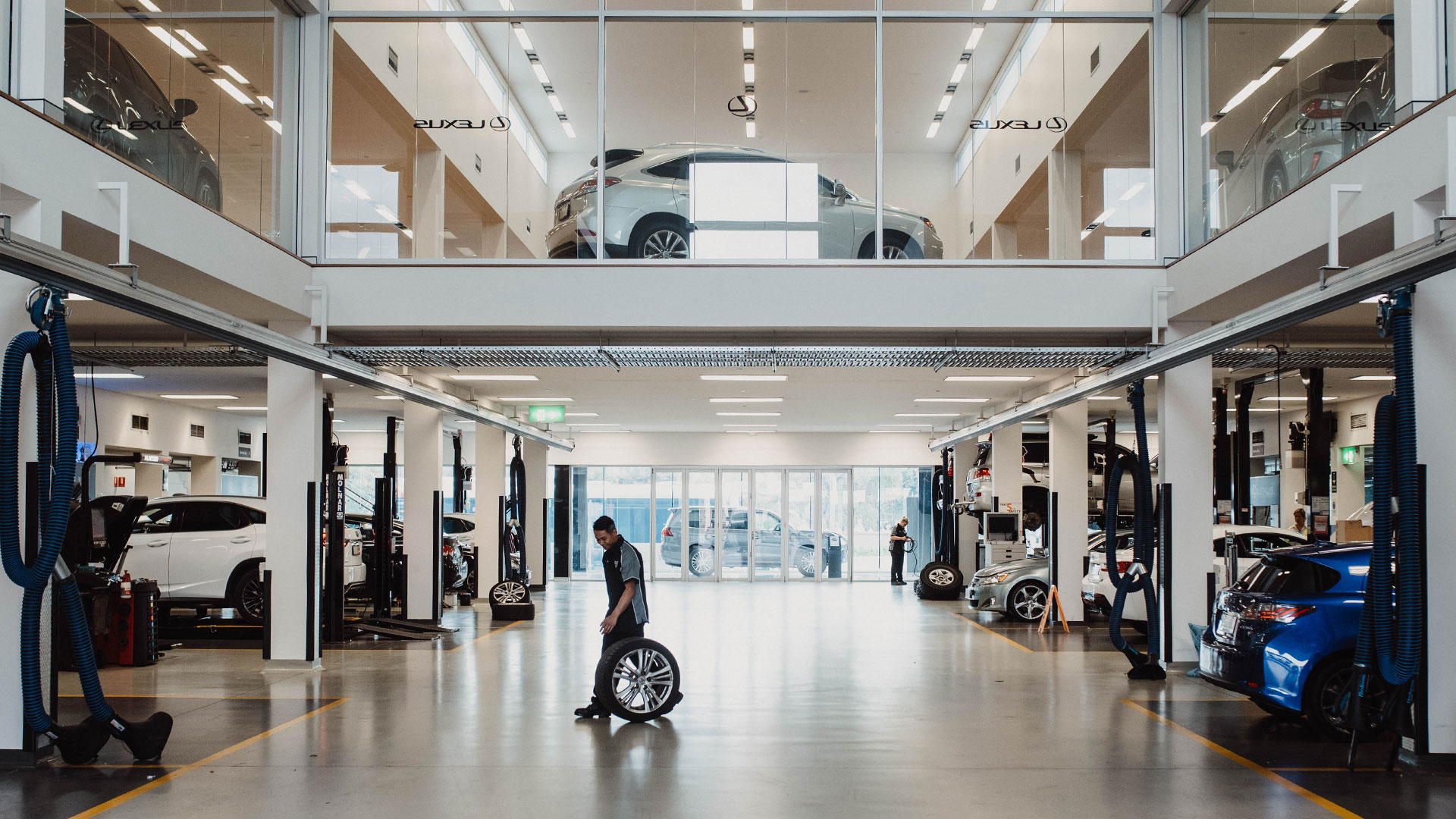 A hallway inside a Lexus servicing center, as a man holding a wheel walks across the way.