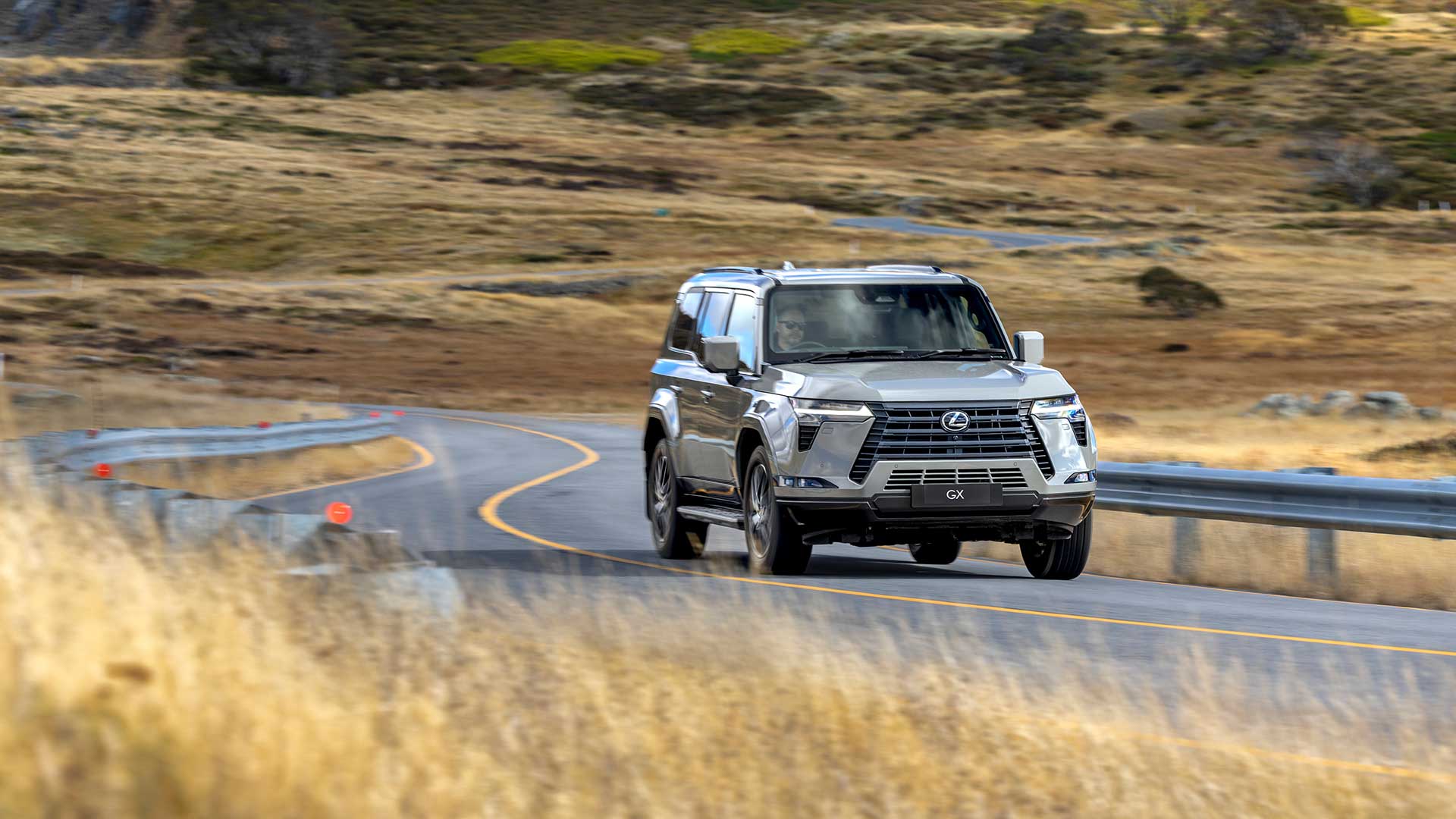 Lexus GX driving on a windy country road with dry grass in the background