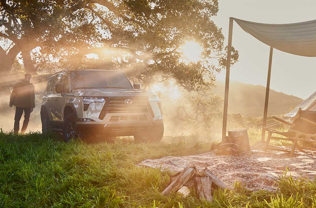 The Lexus GX on grass, parked next to a campsite with owner walking beside it.