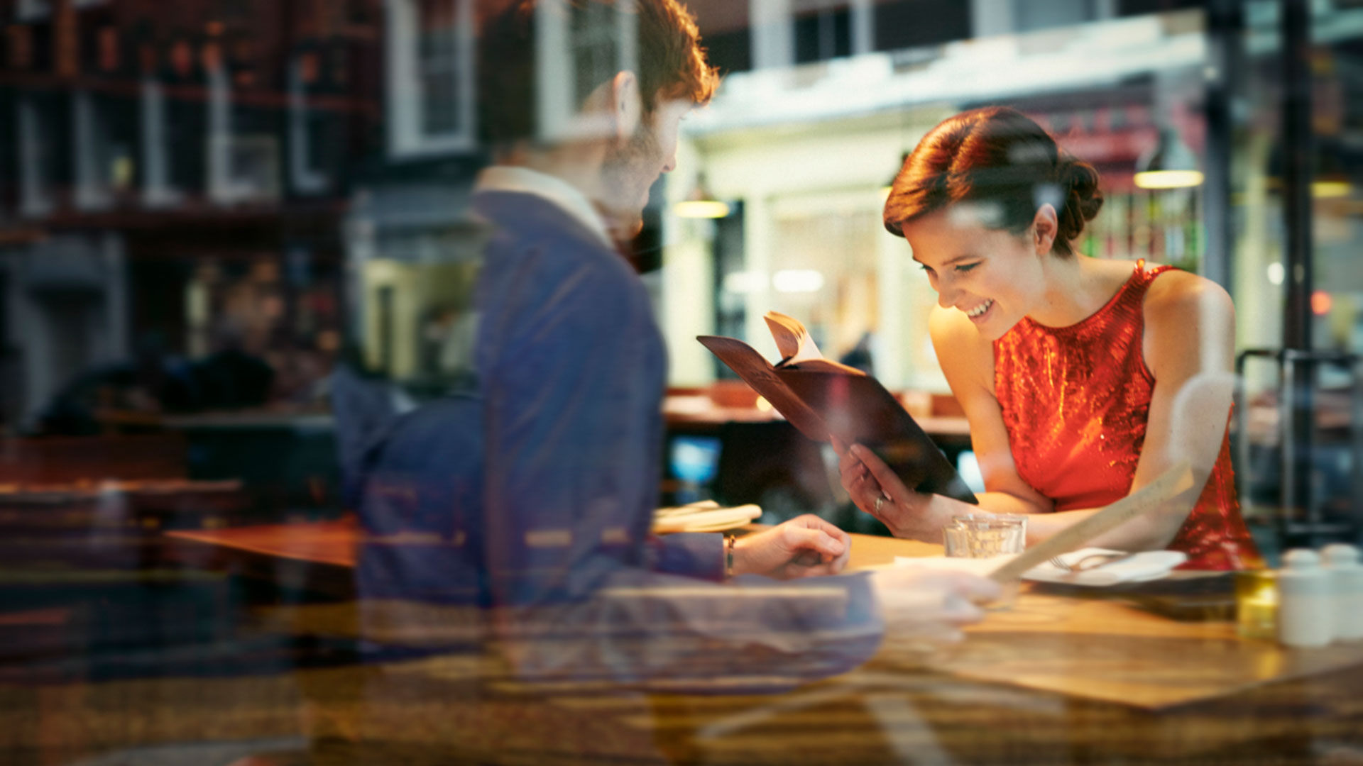 A woman smiles as she reads from a book at a table with a man.