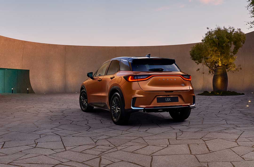 Rear view of a copper Lexus LBX SUV parked in a modern courtyard at dusk.