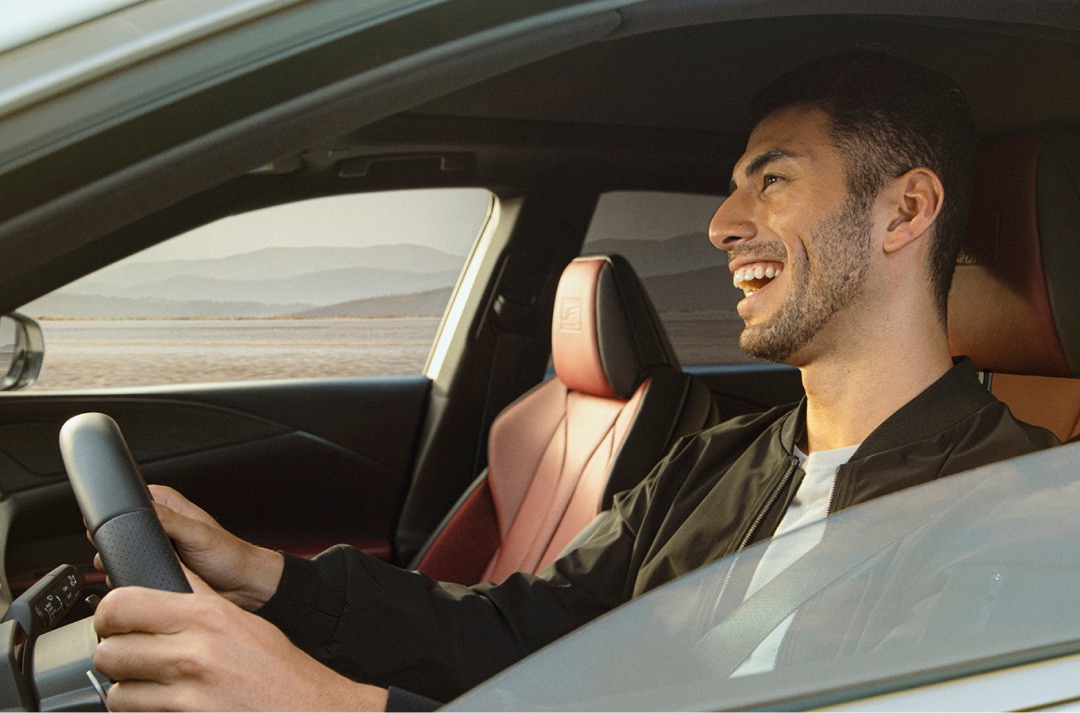 Smiling man drives 2022 RX F Sport, hands on wheel. Distant mountains visible through passenger window.