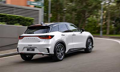 White Lexus LBX compact SUV driving through a city street, rear three-quarter view